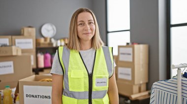 Mutlu, kendinden emin, güzel gülümseyen genç bir sarışının portresi. Bir hayır kurumunda gönüllü olarak çalışıyor. Yansıtıcı bir yelek giyiyor.