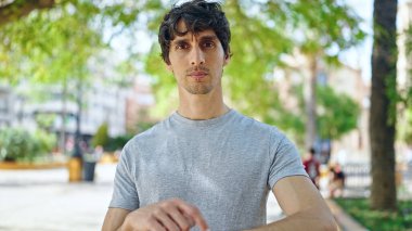 Genç İspanyol adam parkta ciddi bir yüzle izlemeyi işaret ediyor.