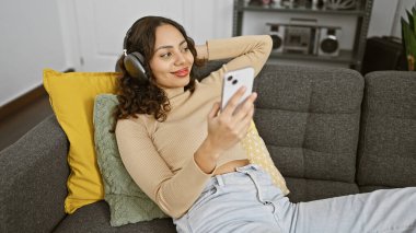 Rahat, melez bir kadın. Kanepede uzanıyor. Kulaklıklı bir akıllı telefon kullanıyor.