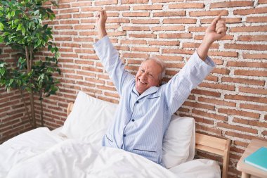 Middle age grey-haired man waking up stretching arms at bedroom