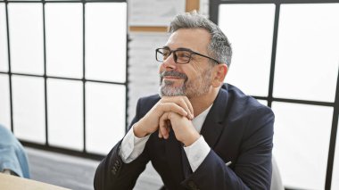 Beyaz saçlı, kendine güvenen İspanyol bir adam rahat bir ofis işyerinde oturmuş iş fikirlerinden şüphe ediyor..