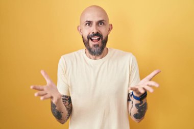 Sarı arka planda dikilen İspanyol dövmeli adam. Kollarını açıp gülümsüyor. Dostça karşılama, olumlu ve kendinden emin selamlar. 