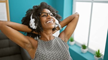 Afrika kökenli Amerikalı iş kadını müzik dinliyor. Elleri ofiste rahat.