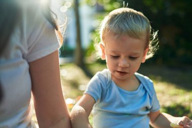 Anne ve oğlu parkta rahat bir ifadeyle bankta oturuyor.