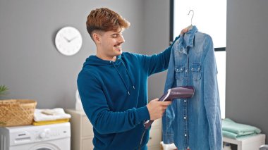 Çamaşır odasında dikey demir makinesiyle gömlek ütüleyen İspanyol genç adam.