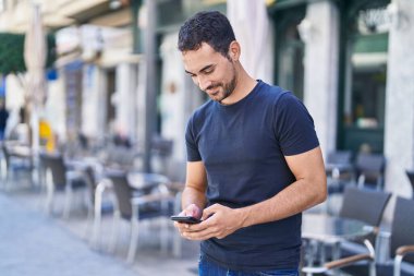 Young hispanic man smiling confident using smartphone at coffee shop terrace