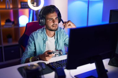Young hispanic man streamer playing video game using joystick at gaming room