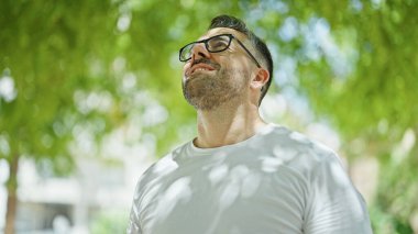 Gri saçlı, gülümseyen, kendine güvenen, parktaki gökyüzüne bakan adam.