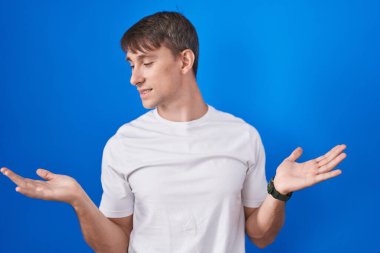 Mavi arka planda duran beyaz tenli sarışın adam avuçlarını açıp gülümsüyor, sunuyor ve reklam karşılaştırması yapıyor ve dengeyi sağlıyor. 