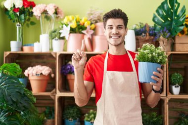Çiçekçi dükkanında çalışan genç İspanyol bir adam elinde çiçekle gülümseyen bir fikir ya da soruyla mutlu bir yüzü işaret eden bir numara. 