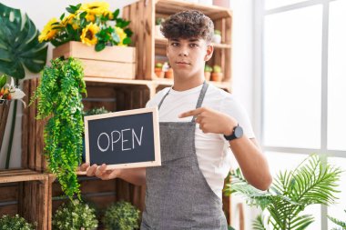 Çiçekçide çalışan İspanyol genç elinde açık tabela, mutlu bir şekilde el ve parmağıyla işaret ediyor. 