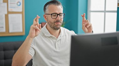 Gri saçlı iş adamı ofiste bilgisayar ararken şans diliyor.