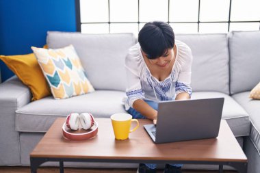 Middle age chinese woman using laptop drinking coffee at home
