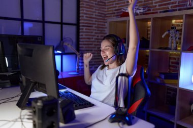 Young caucasian woman streamer playing video game with winner expression at gaming room