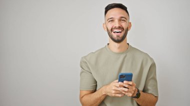 Genç İspanyol adam, izole edilmiş beyaz arka planda gülümseyen akıllı telefon kullanıyor.