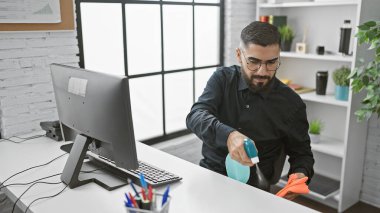 Bearded man cleaning office desktop with disinfectant spray and gloves clipart