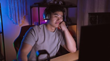 Kulaklık takan Asyalı genç bir adam, loş bir oyun odasındaki bilgisayar ekranına dikkatle bakıyor..