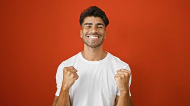 Neşeli bir İspanyol, izole edilmiş bir kırmızı duvara karşı yumruklarını sıkarak kutluyor..