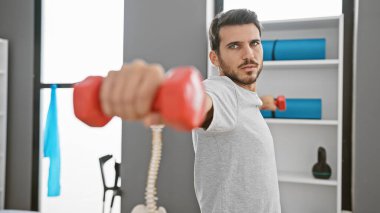 Genç bir İspanyol adam modern bir rehabilitasyon kliniğinde dambılı kaldırıyor. Güç, iyileşme ve sağlık hizmetlerini tasvir ediyor..