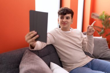 Kanepede oturan, dokunmatik ped kullanan, mutlu gülümseyen, eli ve parmağı yan olan genç, ikiyüzlü olmayan bir adam. 