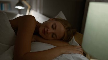 Genç sarışın kadın yatakta uzanıyor, yatak odasında uyuyor.