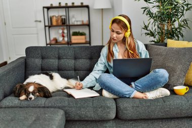 Kanepede oturan beyaz bir kadın ve evde ders çalışan bir köpek.