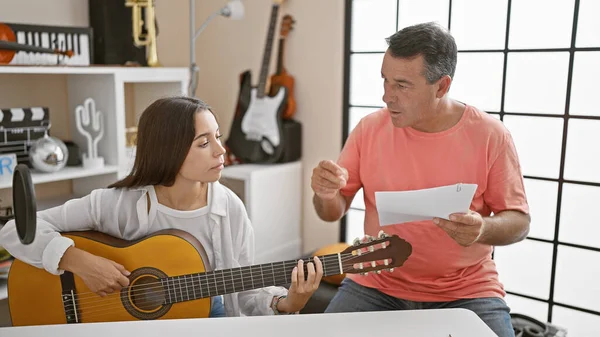 Hispanic man and woman musicians delight in a classic guitar melody at a music studio, concentrating in the serene ambience filled with the essence of spanish classical tunes