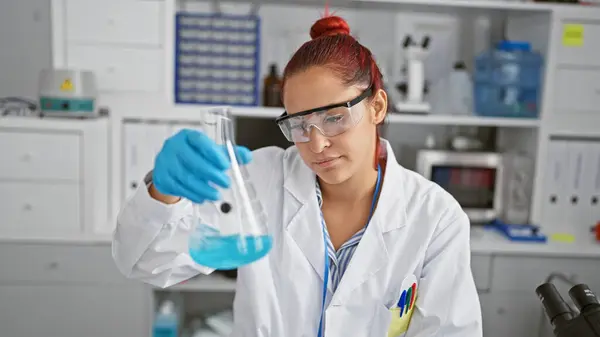 Brilliant young redhead woman scientist engrossed in medical research, meticulously measuring liquid in a test tube, security gloves on, at the busy heart of a bustling laboratory.