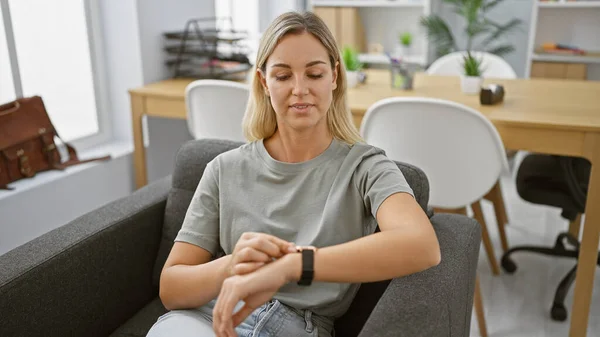Young Blonde Woman Checks Smartwatch Modern Office Showcasing Technology Punctuality — Stock Photo, Image