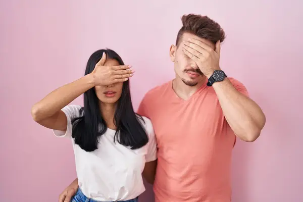 Young Hispanic Couple Standing Pink Background Covering Eyes Hand Looking — Stock Photo, Image