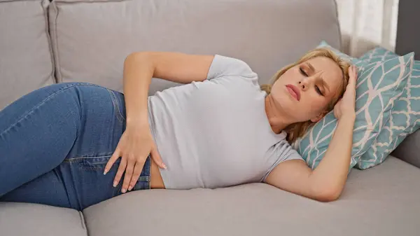 Young Blonde Woman Suffering Menstrual Pain Lying Sofa Home — Stockfoto