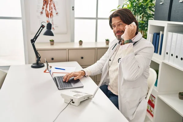 Middle Age Man Doctor Using Laptop Talking Telephone Clinic — Stock Photo, Image