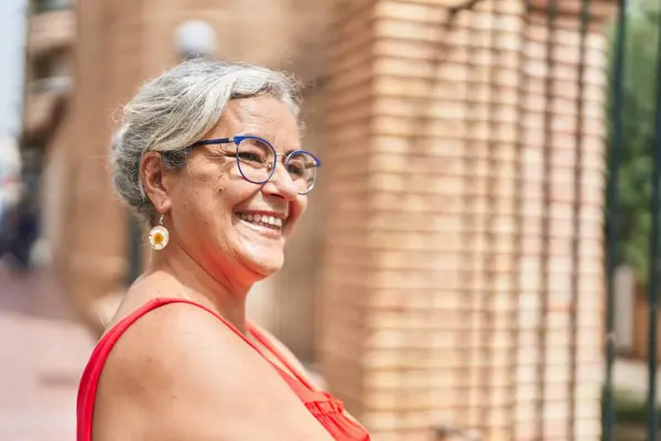 Middle age grey-haired woman smiling confident looking to the side at street