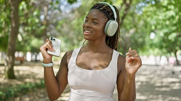 Parkta gülümseyen müzik dinleyen Afrikalı Amerikalı kadın.