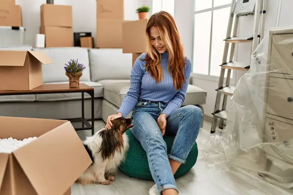 Young caucasian woman smiling confident sitting on floor with dog at new home