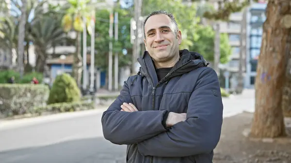Knappe Spaanse Man Met Gekruiste Armen Glimlachend Een Stadspark Omringd — Stockfoto
