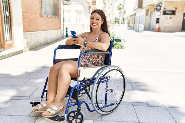 Genç ve güzel İspanyol kadın akıllı telefon kullanıyor. Sokakta tekerlekli sandalyede oturuyor.