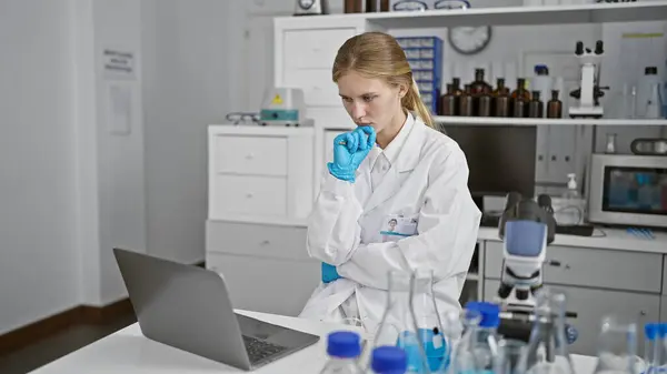 Thoughtful woman scientist analyzing data on laptop in laboratory