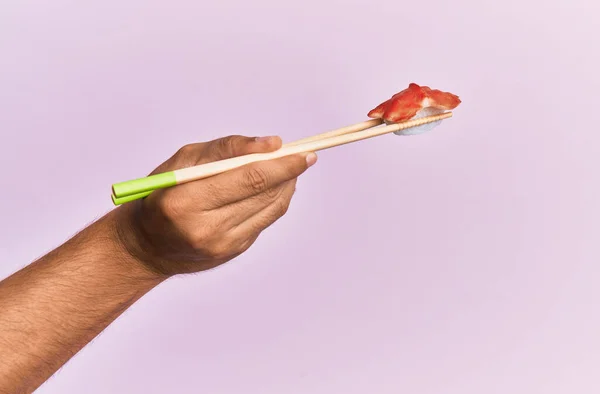 Hand of man holding octopus nigiri with chopsticks over isolated pink background