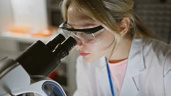 Blonde woman scientist using microscope in laboratory setting, showcasing research, healthcare and educational concepts.