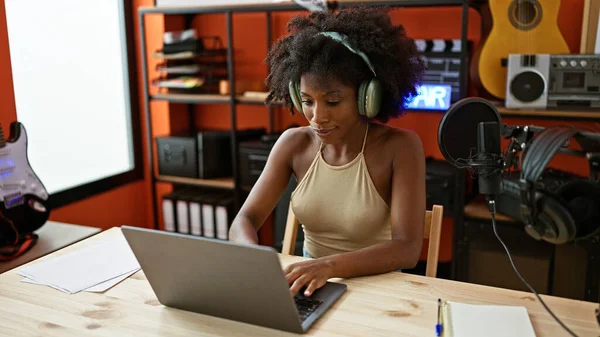 stock image African american woman musician using laptop and headphones at music studio