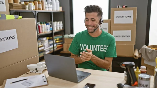 Young, attractive hispanic man, clapping in applause, volunteers his computer skills at a charity center, while sitting and listening through headphones.