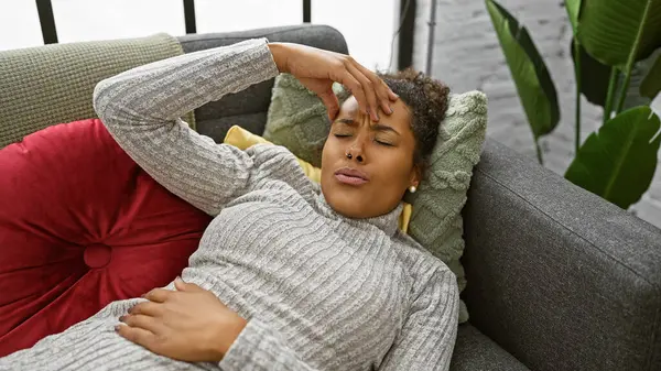 Kendini kötü hisseden genç bir kadın, evdeki kanepede uzanmış, eli alnında..