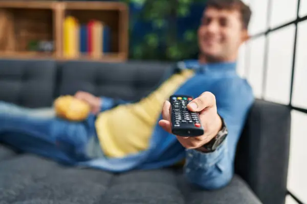 Young hispanic man watching movie lying on sofa at home