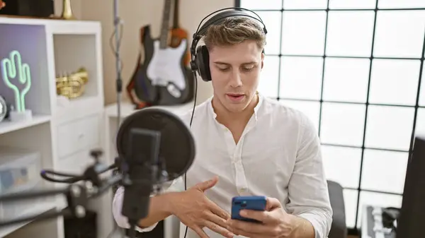 Handsome young caucasian man, professional radio reporter, on air, speaking and reading news from smartphone screen in radio studio