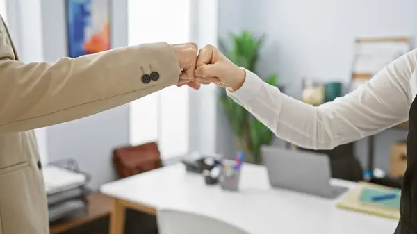 stock image Two coworkers performing a fist bump in an office setting, signifying teamwork and partnership.