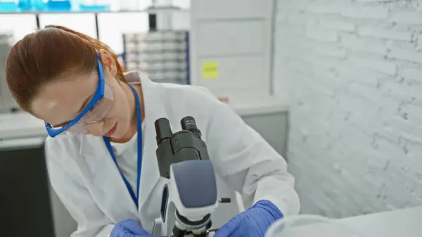Zogniskowana Biała Kobieta Okularach Ochronnych Bada Próbkę Przez Mikroskop Pomieszczeniach — Zdjęcie stockowe