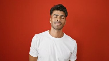 Sakallı, gülümseyen, genç bir İspanyol 'un portresi, canlı kırmızı bir duvara karşı duruyor, beyaz bir gömlek giyiyor..