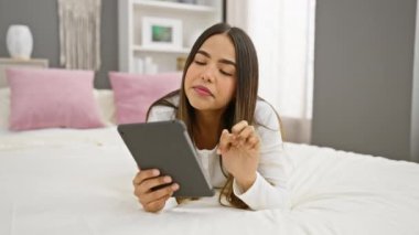 İspanyol kadın rahat, modern bir yatak odasında tabletle rahatlıyor.