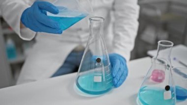 Laboratuvar önlüklü bir bilim adamı deney şişesinden kapalı bir şişeye kimyasal döküyor..